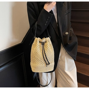 Detail of woven straw bucket bag with hollow diamond pattern and black leather drawstring