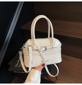 Close-up of cream-white shell bag with pebble leather texture and metal buckle detail