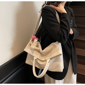 Detalle de bolso tote beige en piel granulada con bandolera y colgante de perrito