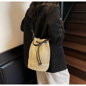 Detailed view of hand-woven straw bucket bag with black leather drawstring on model