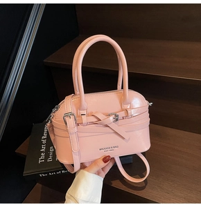Detail of light pink glossy shell bag featuring decorative strap knot and metal buckle clasp