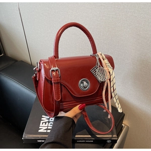 Close-up of red oil wax leather handbag with silver lock and decorative scarf pendant