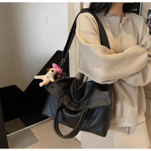 Detalle de bolso tote negro de cuero granulado con colgante de perro de peluche