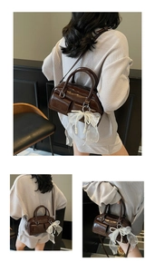 Detail of dark brown glossy leather Boston bag with decorative lace bow and pearl charm