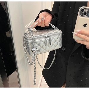 Detail of silver quilted vanity case bag featuring a metal chain strap and spherical charm