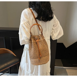 Model wearing a hollow woven straw bucket bag with brown leather drawstring and strap details