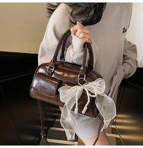 Detail of dark brown patent leather Boston bag with pearls and organza bow charm