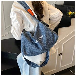 Dettaglio della grande borsa tote in denim con etichetta arancione e logo su modello
