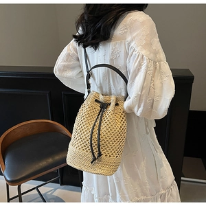 Close-up of beige woven bucket bag with black leather drawstring and strap on model