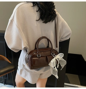 Detail of dark brown patent leather Boston bag with white lace and pearl bow charm