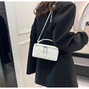 Detail view of quilted white crossbody box bag with silver chain strap on model