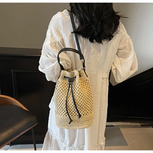 Detail of hollow woven bucket bag with black leather drawstring and shoulder strap worn by model