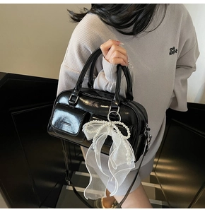 Detail of black glossy patent leather Boston bag with pearl mesh bow charm and strap