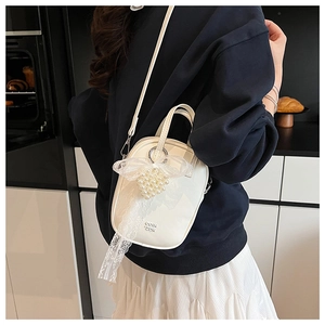 Mini borsa a tracolla bianca con ciondolo di perle e fiocco in pizzo su superficie morbida