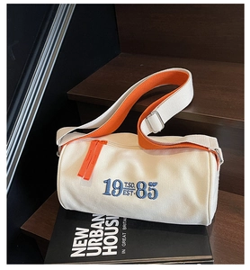 Close-up of vintage canvas cylinder bag with orange strap and 1985 embroidery detail