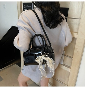 Detail of black patent leather bag featuring front flap pockets and white lace bow charm