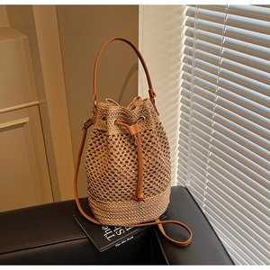 Detail of hollow woven straw bucket bag with brown leather handle and drawstring closure