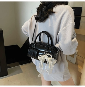 Detail of black patent leather boston bag with white lace pearl bow charm decoration