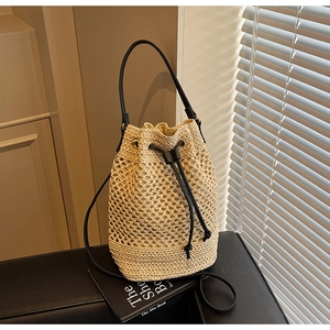 Detail of hollow woven straw bucket bag with black leather drawstrings and handles