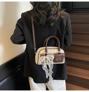 Detail view of cream and brown Boston bag featuring lace pearl bow charm on a model
