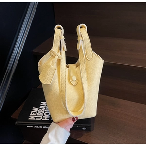 Detail view of light yellow litchi pattern leather bucket bag with top handles and charm