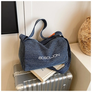 Dettaglio della borsa tote in denim con ricamo BOSOLJON su una valigia argento