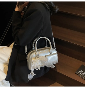 Detail showing metallic silver Boston bag with pearl and white bow tie on the front pocket