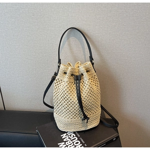 Close-up of woven straw bucket bag showing hollow patterns and black leather drawstring