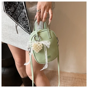 Dettaglio borsa a tracolla verde menta con ciondolo a cuore di perle e fiocco in pizzo