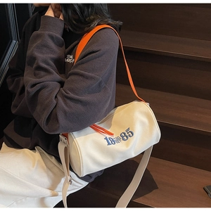 Close-up of cream canvas tote bag with orange zipper and blue embroidered text on stairs