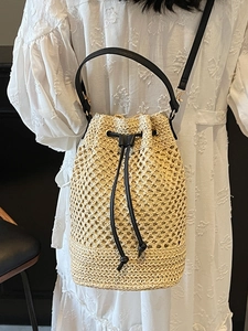Hollow woven straw bucket bag with black drawstring closure and shoulder strap for women