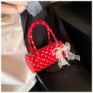 Close-up of a red polka dot Boston bag featuring a white pearl and lace bow charm detail