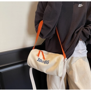 Detail view of cylinder canvas tote bag featuring orange zipper and blue side embroidery