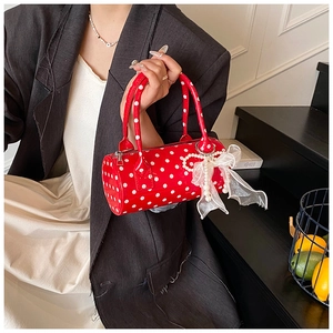 Detail of red polka dot cylinder handbag with pearl lace bow charm and glossy leather texture