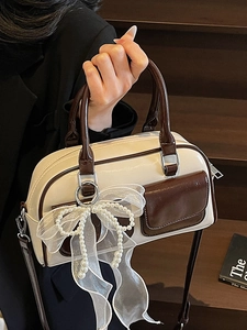 Chic beige Boston handbag with brown trim and pearl bow charm shown in lifestyle setting