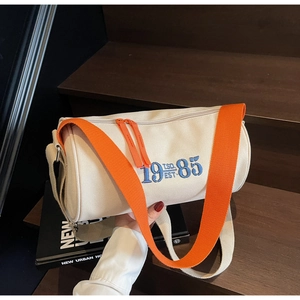 Close-up of cream canvas barrel bag with orange straps and 1985 EST embroidery