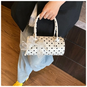 Detailed shot of white polka dot cylinder handbag featuring a pearl lace bow charm