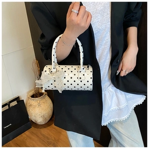 Close-up of a white cylindrical polka dot handbag with a delicate lace bow charm detail