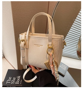 Detail of cream leather bucket bag with silk scarf handle and golden hardware