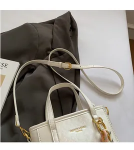 Detail of minimalist cream bucket bag with gold lettering and adjustable shoulder strap