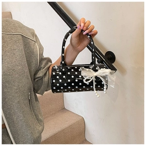 Macro detail of black polka dot boston bag with white lace bow and pearl chain