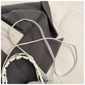 Detail of white mesh handbag with black polka dot handle on a grey suit jacket background