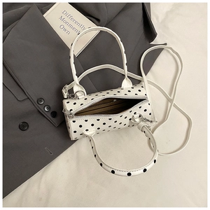 Close-up of white polka dot cylinder bag with silver zipper and striped lining