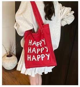 Close-up of red canvas tote bag with white HAPPY print worn by model in casual setting