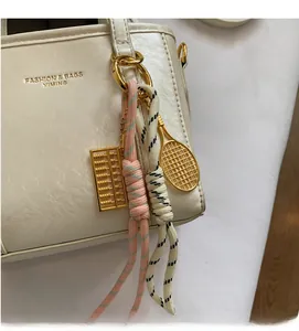 Close-up of cream handbag detail featuring golden abacus, tennis racket and woven charms
