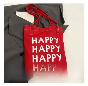 Detail of red canvas tote bag with white HAPPY text lettering on grey blazer backdrop