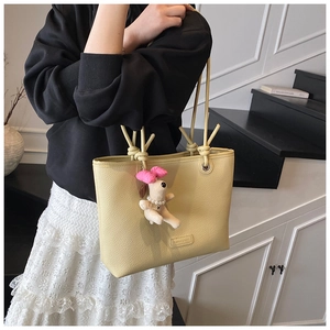 Pale yellow leather tote bag with a cute white puppy plush charm shown on shoulder