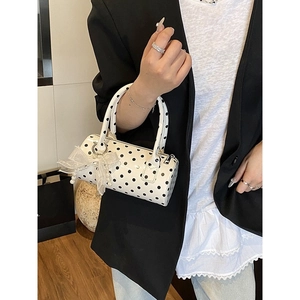 Chic white polka dot Boston handbag with pearl lace bow charm held by a model in a suit