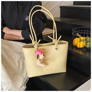 Detail of yellow pebbled leather tote bag with knot handles and cute puppy charm accessory
