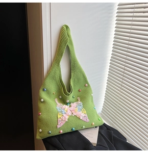 Detail of green knitted tote bag with colorful beads and 3D pink butterfly floral accent